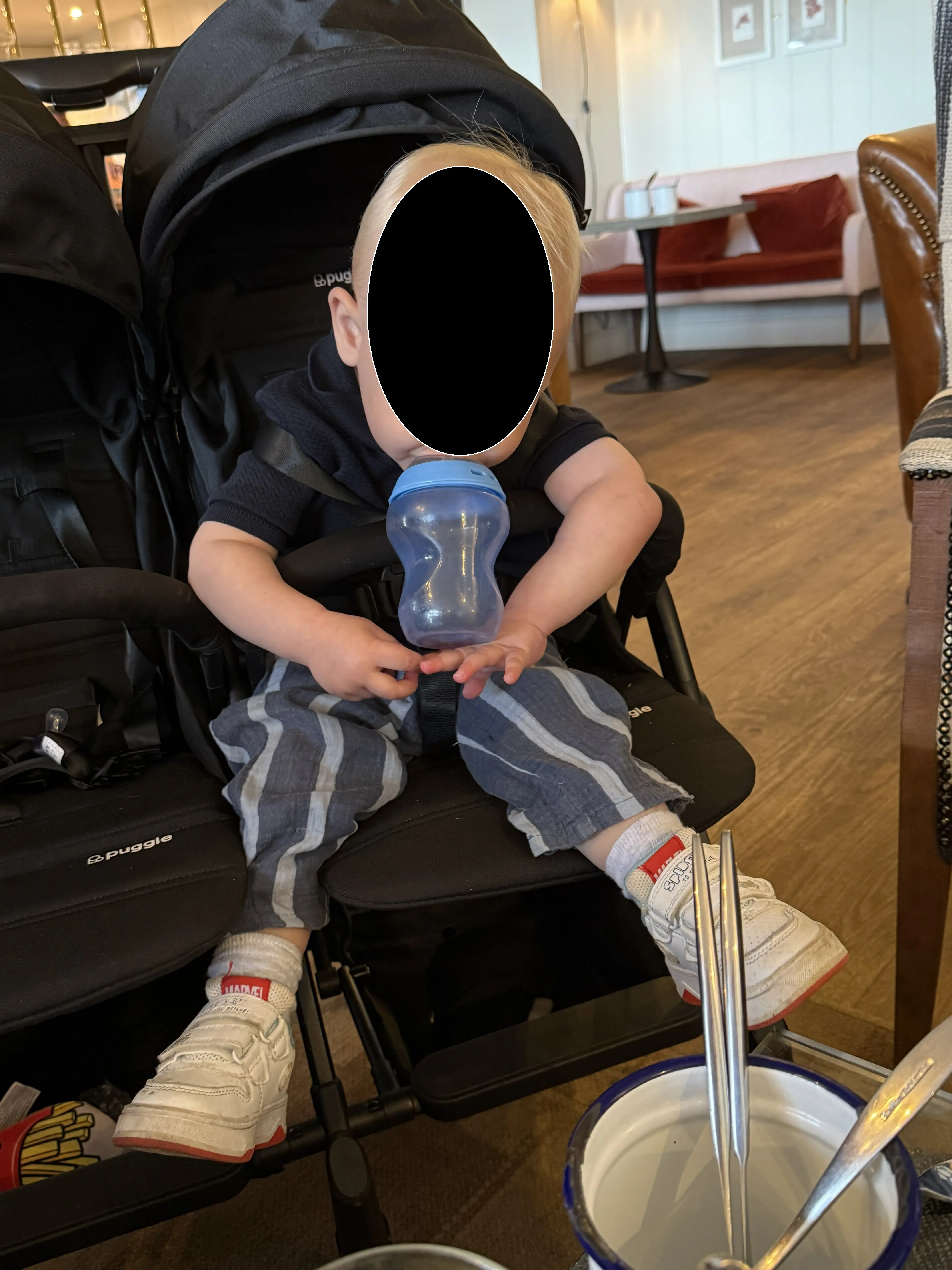 Toddler in Puggle City Traveller double pushchair seat at restaurant, second seat visible alongside, Puggle branding on frame